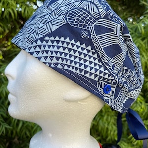 May include: A blue and white patterned surgical scrub hat with a white button and blue ties. The pattern features a geometric design with a turtle.