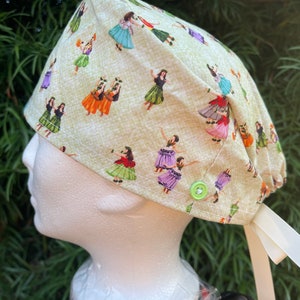 May include: A green and white patterned surgical scrub hat with a green button and a white ribbon tie. The hat features a repeating pattern of hula dancers.