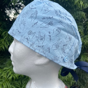 May include: Light blue scrub hat with a pattern of hand gestures and phrases like "it's all good", "take my hand", "you got this", "good job", "i love you", and "peace".