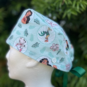 May include: A green scrub hat with a white button and green ties. The hat features a repeating pattern of tropical leaves, flowers, and characters from the animated film Moana.