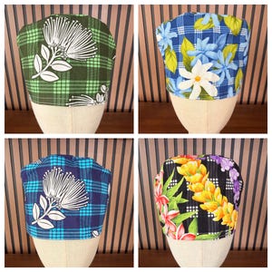 May include: Four scrub caps displayed on mannequin heads. The top left features a green plaid pattern with white floral motifs. The top right shows a blue plaid background with white and blue flowers. The bottom left is a blue plaid with white floral designs. The bottom right displays a black plaid with yellow and pink tropical flower patterns.