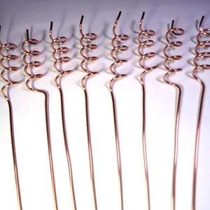 Könnte beinhalten: Sieben Kupferstifte mit einer Spiralform an der Spitze. Die Stifte sind gerade und haben eine glatte, metallische Oberfläche.