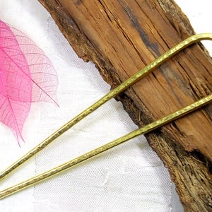 Può includere: Un fermaglio per capelli in ottone martellato con un design a forma di U. Il fermaglio è di un caldo colore oro e ha una superficie strutturata. L'accessorio per capelli è esposto su un pezzo di legno.