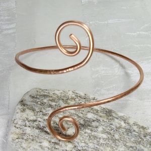 Può includere: Un braccialetto in filo di rame con due motivi a spirale. Il braccialetto è martellato per la texture.