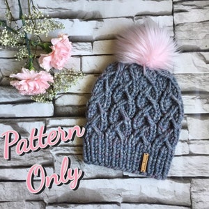 May include: A gray knitted hat with a pink faux fur pom pom. The hat has a cable knit pattern and a small brown leather tag with the word "Handmade" on it. The text "Pattern Only" is written in pink letters on a gray background.