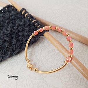 May include: A gold bangle bracelet with a magnetic clasp and a row of peach-colored square beads.