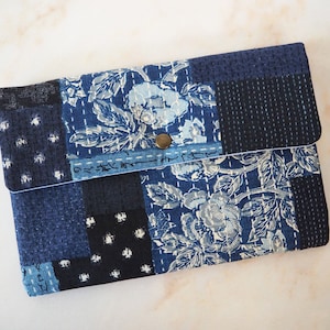 Peut inclure: Une pochette en tissu patchwork bleu et blanc avec un motif floral et une fermeture à bouton unique.