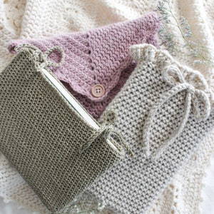 Peut inclure: Trois housses de livres en crochet de différentes couleurs et styles. Les housses sont réalisées avec une variété de points et de textures. Les housses sont présentées sur une couverture en crochet blanche.