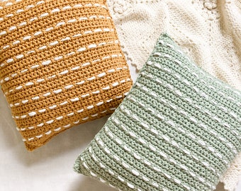 May include: Two crocheted throw pillows, one mustard yellow and one sage green, with white stitching. The pillows are on a white crocheted blanket.