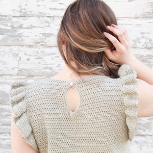 May include: A crocheted top with a keyhole back and ruffled sleeves. The top is a light beige color.