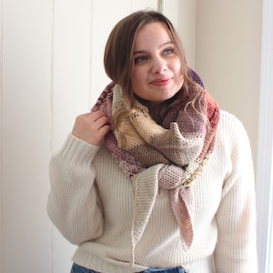 May include: A woman wearing a white sweater and blue jeans with a multi-colored knitted scarf around her neck.