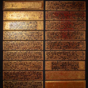 Puede incluir: Una colección de páginas de manuscritos antiguos rectangulares, doradas y marrones. Las páginas están cubiertas de texto oscuro e intrincado, algunas con bordes decorativos. La disposición sugiere un artefacto histórico o cultural.