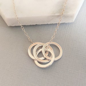 Puede incluir: Collar de plata con un colgante de tres círculos entrelazados.