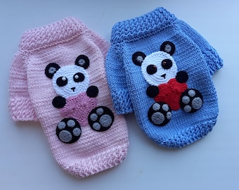 May include: Two knitted dog sweaters, one pink and one blue, each with a panda bear applique holding a heart.