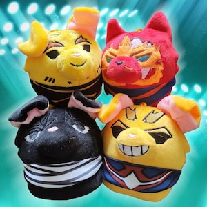 May include: Four plush toys in the shape of animal heads. The toys are yellow, red, black, and yellow with black and red accents. The toys are all smiling and have large eyes.
