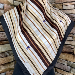 May include: A white silk scarf with brown and beige stripes and a black border. The scarf has three purple bows and the text "Roberta di Camerino" in the bottom corner.