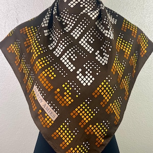 Puede incluir: Pañuelo cuadrado marrón con un patrón geométrico repetido en blanco, amarillo y naranja. El pañuelo está drapeado sobre un maniquí. La etiqueta "HARDY AMIES" es visible.