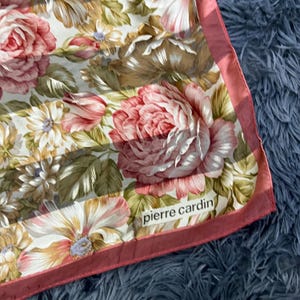 Puede incluir: Pañuelo floral con grandes rosas rosas y rojas, con acentos de hojas blancas y verdes. El pañuelo tiene un borde rojo y el logo "pierre cardin".