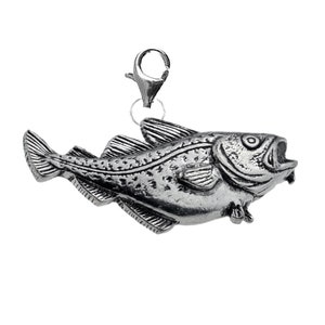 May include: A silver charm in the shape of a cod fish with a detailed design. The charm has a lobster clasp for attaching to a bracelet or necklace.