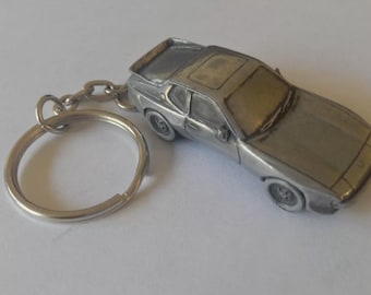 May include: A silver metal keychain featuring a detailed model of a classic sports car. The car has a sunroof and a key ring attached.