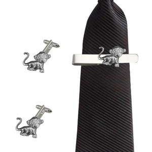 May include: A set of silver monkey cufflinks and a matching tie bar. The tie bar is attached to a black striped tie.