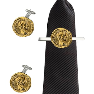 Puede incluir: Un juego de gemelos y un pasador de corbata dorados con un diseño de moneda romana. El pasador de corbata está sujeto a una corbata negra a rayas.