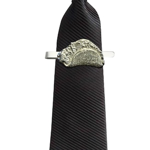 May include: A black tie with a silver tie clip featuring a detailed design. The tie clip is attached to the tie.