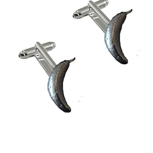 May include: A pair of silver cufflinks with a banana design. The bananas are silver and have a realistic texture.