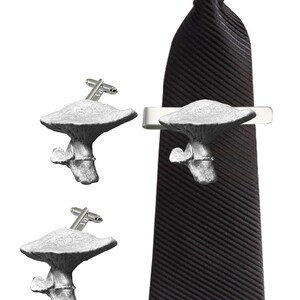 Puede incluir: Un juego de gemelos y un clip para corbata con forma de hongo. Los gemelos y el clip para corbata están hechos de metal plateado y presentan un diseño de hongo detallado.