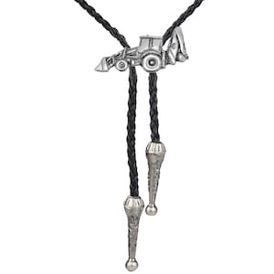 May include: A black bolo tie with a silver tractor charm. The bolo tie has two silver tips with a textured design.