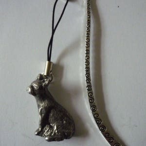Puede incluir: Marcapáginas de plata con una pequeña figura de perro sentado de estaño detallada. El marcapáginas tiene una cuerda negra atada a la parte superior.