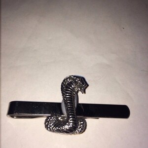 May include: A silver tie clip featuring a cobra snake design.