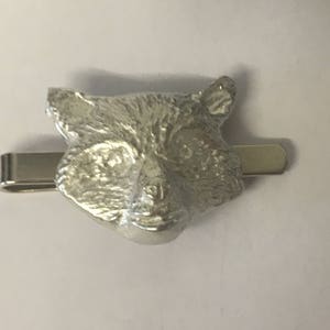 May include: A silver tie clip featuring a detailed raccoon head design.