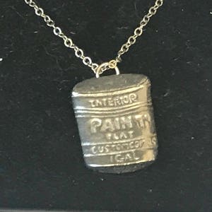May include: Silver necklace with a paint can pendant. The can has the words "Interior Paint Flat Custom Colors Ideal" printed on it.