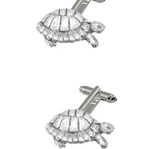 May include: A pair of silver cufflinks featuring a detailed turtle design. The turtle is depicted in a walking position with its head raised.