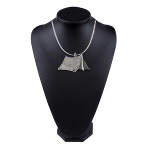 May include: A silver necklace with a tent-shaped pendant. The pendant is detailed and has a textured surface.