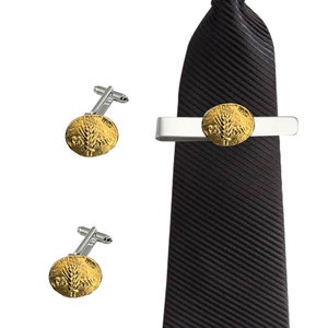 Puede incluir: Un juego de gemelos y pasador de corbata de oro con un diseño de trigo. El pasador de corbata está sujeto a una corbata negra.