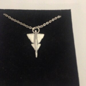 May include: A silver necklace with a pendant shaped like a stylized airplane. The pendant is detailed with lines and angles.
