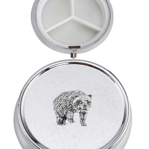 May include: A silver pill box with a bear design on the lid. The box has three compartments inside.