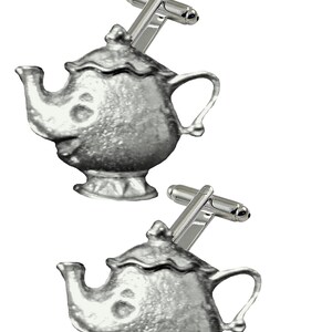 Może przedstawiać: Para srebrnych spinek do mankietów, każda w kształcie czajniczka z uśmiechniętą twarzą. Czajniczki mają uchwyt, dzióbek i pokrywkę. Spinki do mankietów mają srebrny drążek do mocowania do mankietu koszuli.