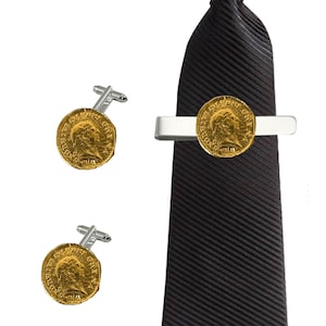 Puede incluir: Un juego de gemelos dorados y un pasador de corbata con un diseño de moneda romana. El pasador de corbata es plateado y tiene una corbata negra.