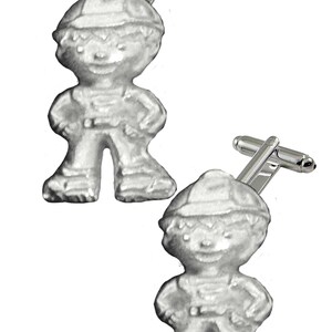 Op de afbeelding: Een paar zilveren manchetknopen met een cartoonjongen die een hoed en een overall draagt. De manchetknopen zijn een leuke en unieke accessoire voor elke gelegenheid.