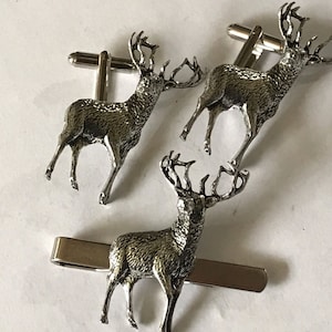 May include: A set of three silver stag cufflinks and a matching tie bar. The stag cufflinks are detailed with antlers and the tie bar features a stag with antlers.