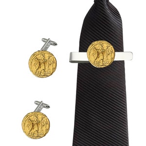 Op de afbeelding: Een set gouden manchetknopen en een stropdasclip met een replica van een Romeinse munt met de inscriptie "CAE.SAR". De stropdasclip is bevestigd aan een zwarte stropdas.