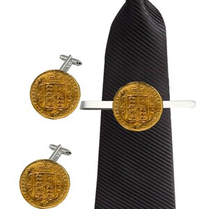 Puede incluir: Un juego de gemelos y pasador de corbata de oro con una réplica de una moneda de oro británica. El pasador de corbata está sujeto a una corbata negra a rayas.