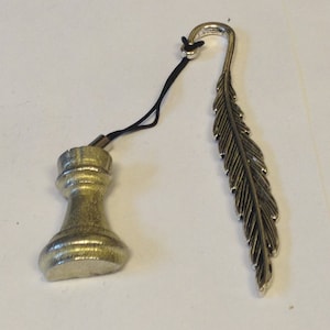 Puede incluir: Un marcapáginas de plata con forma de pieza de ajedrez con un diseño de pluma. La pieza de ajedrez es un peón y la pluma está detallada con líneas.