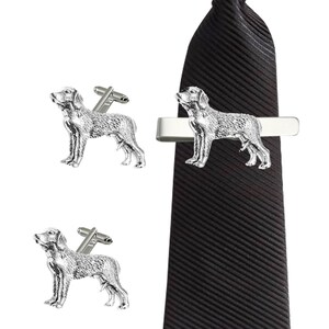 May include: A set of silver cufflinks and a tie bar featuring a detailed dog design. The tie bar is attached to a black striped tie.