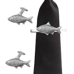May include: A set of silver fish cufflinks and a matching tie bar. The tie bar is attached to a black tie.