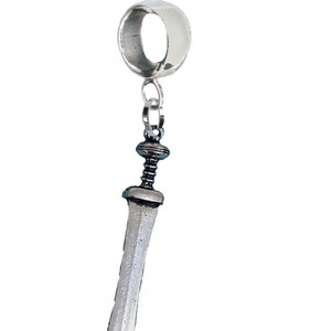 May include: A silver-colored charm featuring a miniature Roman gladius sword pendant. The sword has a detailed hilt and a slightly curved blade. The charm is suspended from a ring-shaped bail.