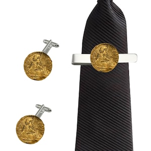 Puede incluir: Un juego de gemelos dorados y un clip de corbata con una réplica de una antigua moneda romana. El clip de corbata está sujeto a una corbata negra.
